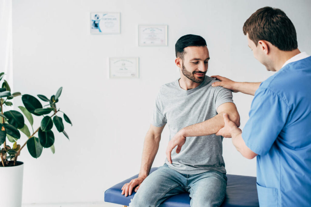 Selective focus of chiropractor examining patient shoulder in massage cabinet at clinic